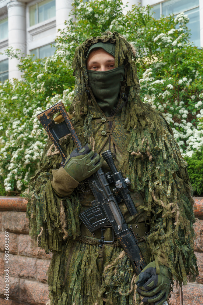Fototapeta premium A soldier in a mask and military equipment with a weapon in his hands. Camouflage clothing on the soldier. A young man armed with a rifle.