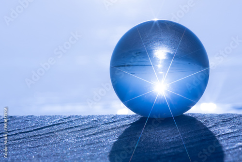 Obraz na plátně A clear glass sphere sits on the sand, reflecting the blue sky and the beach with starburst light effects