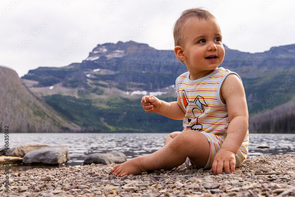 Fototapeta premium Adorable Baby Sitting by a Serene Lake in Waterton, Alberta, Canada with Scenic Mountain View