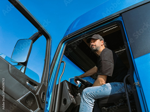 A young man is a professional driver in the cab of a blue truck. Handsome Caucasian guy, a transportation worker sits in a big truck car