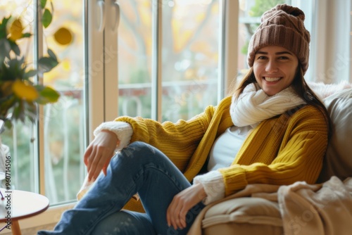 Cozy afternoon at home with a cheerful woman in warm winter attire sitting comfortably on her sofa, embracing the autumn vibes