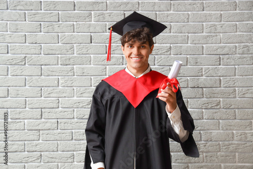 Male graduate student with diploma on grey brick background