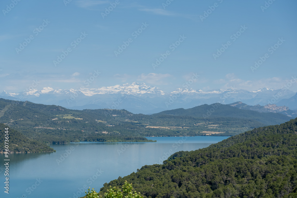 view over beautiful water, hills and distant Pyrenees mountains at Embalse de El Grado Reservoir, blue summer sky, Huesca, Spain view over beautiful water, hills and distant Pyrenees mountains at Embalse de El Grado Reservoir, blue summer sky, Huesca, Spain