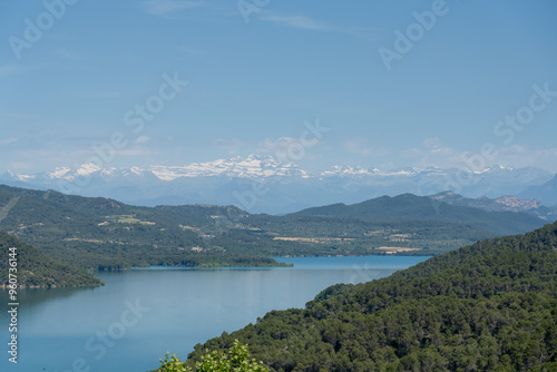 view over beautiful water, hills and distant Pyrenees mountains at Embalse de El Grado Reservoir, blue summer sky, Huesca, Spain