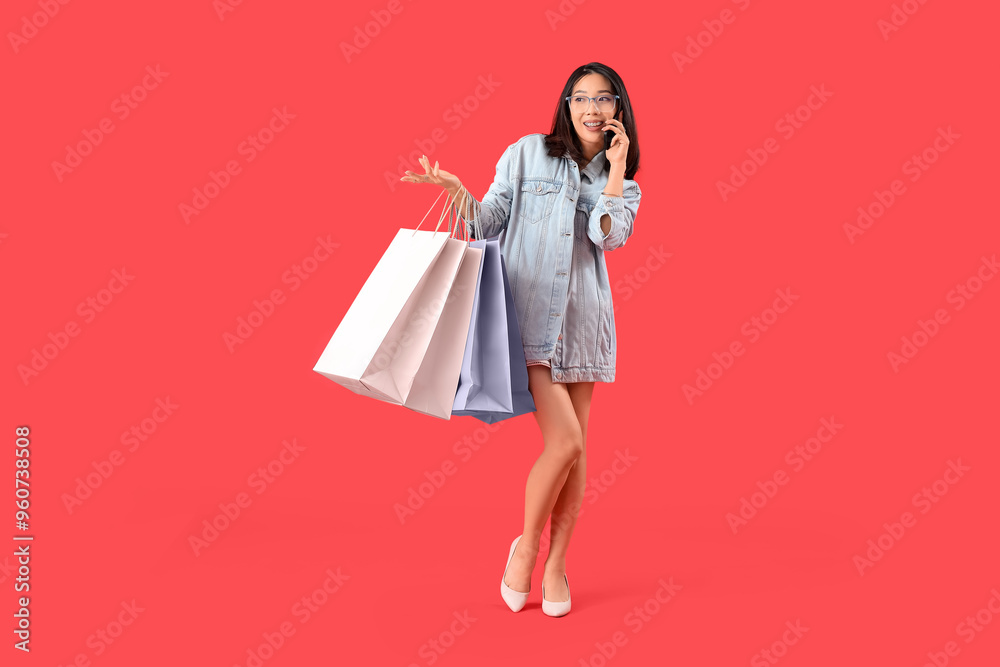 Happy beautiful young Asian woman with shopping bags talking by mobile phone on red background Happy beautiful young Asian woman with shopping bags talking by mobile phone on red background