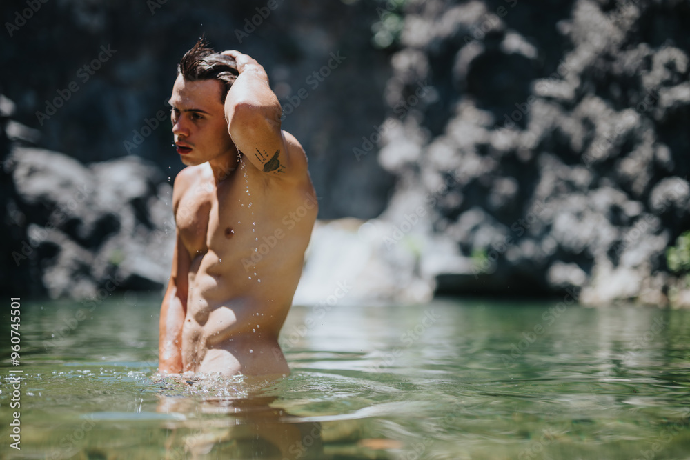 Fototapeta premium A young man stands waist-deep in a clear natural water pool, with rocky cliffs in the background, enjoying a refreshing dip.