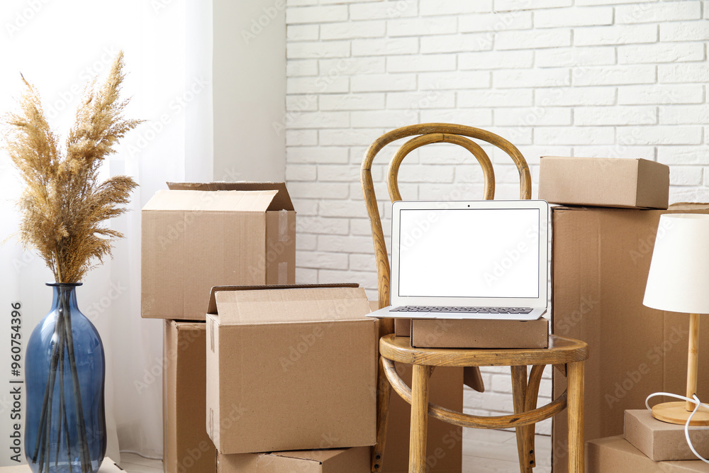 Blank laptop on chair with moving boxes and pampas grass in light room Blank laptop on chair with moving boxes and pampas grass in light room
