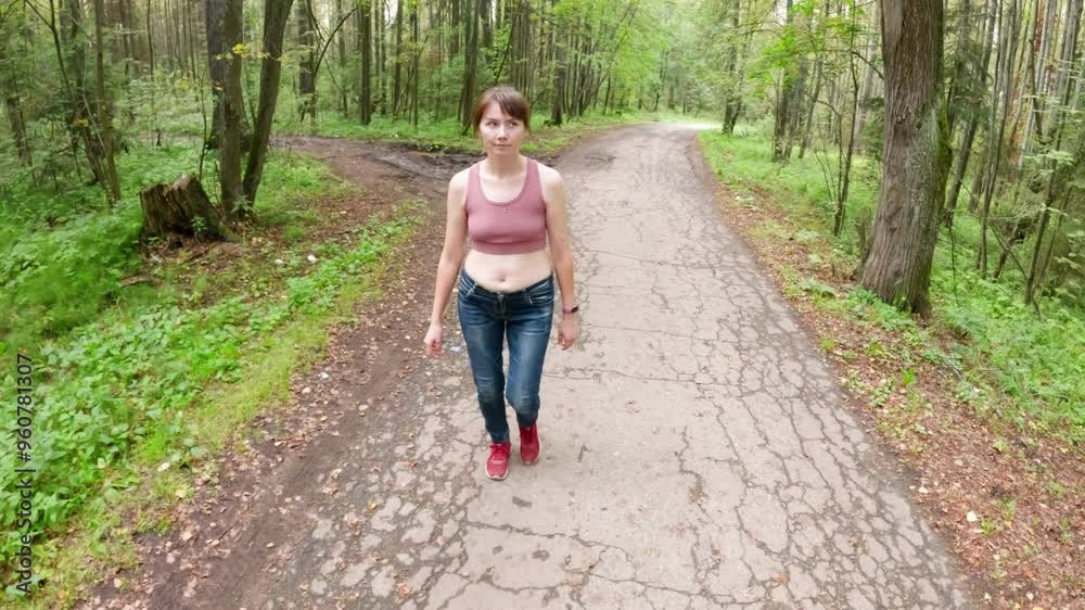 Young woman enjoys a peaceful walk along a quiet path in a lush green forest. Surrounded by trees and sunlight, she embraces the tranquility of nature on a beautiful summer day Young woman enjoys a peaceful walk along a quiet path in a lush green forest. Surrounded by trees and sunlight, she embraces the tranquility of nature on a beautiful summer day