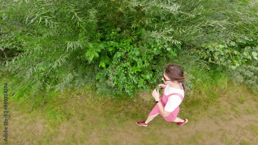 Woman relishes a refreshing walk along a dirt path by a tranquil lake on a bright summer day, enveloped by vibrant greenery and the soothing charm of nature Woman relishes a refreshing walk along a dirt path by a tranquil lake on a bright summer day, enveloped by vibrant greenery and the soothing charm of nature