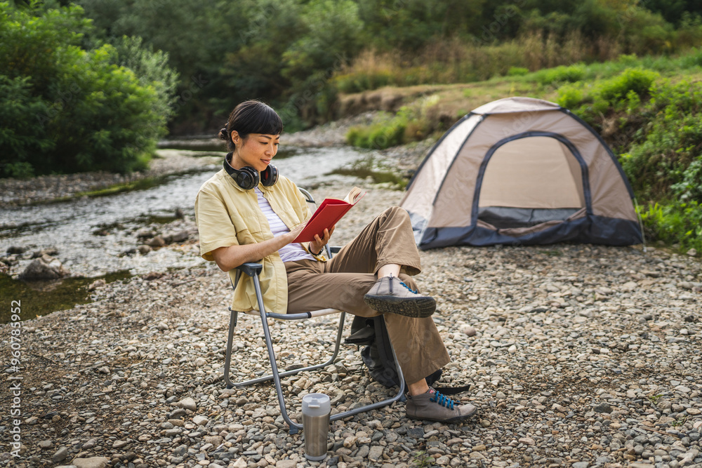 Mature japanese woman sit near river and read a book on camping trip Mature japanese woman sit near river and read a book on camping trip
