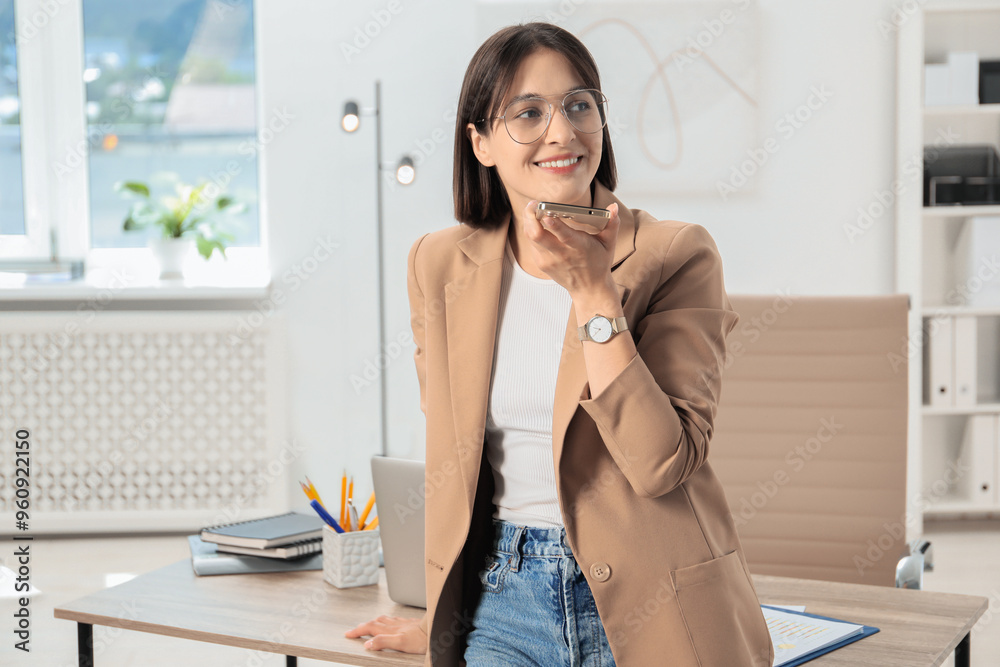 Beautiful woman recording voice message via smartphone in office Beautiful woman recording voice message via smartphone in office