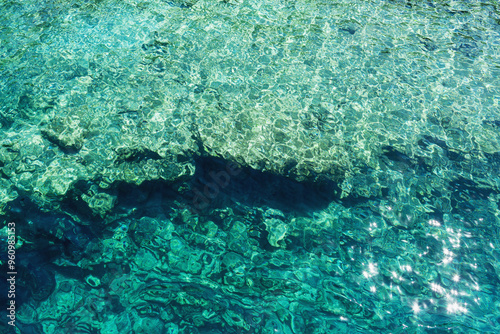 A stunning display of clear turquoise water, creating mesmerizing light patterns as sunlight pierces through, revealing both the depth and clarity of the sea below. Pure natural beauty