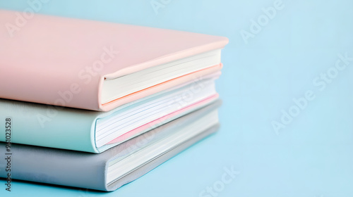 Close-up of a stylish stack of pink, beige, and grey notebooks on a light blue surface, showcasing minimalist and modern stationery design.