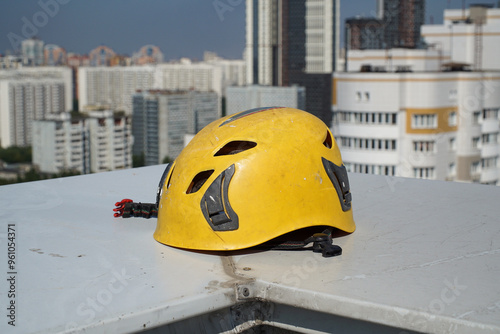 Billede på lærred A climber's helmet lying on the parapet of a high-rise building's roof against the backdrop of a city