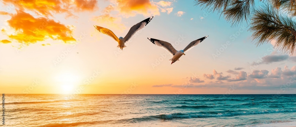 Naklejka premium two seagulls flying against the backdrop of a vibrant sunset over a tranquil ocean.