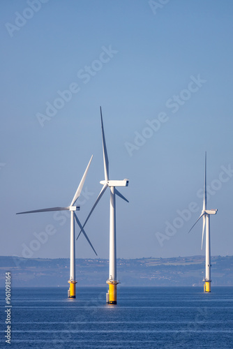 Abstract ethereal view of beautiful giant wind turbines at sea with patchy fog blue sky