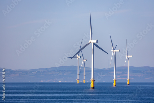 Abstract ethereal view of beautiful giant wind turbines at sea with patchy fog blue sky