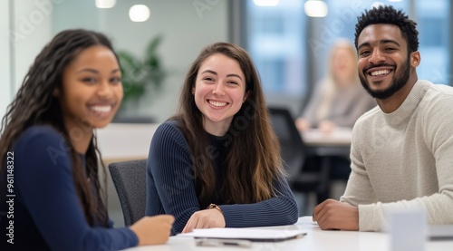 Three diverse young professionals sitting at an office table, smiling and having a meeting.