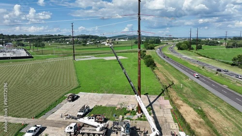 Aerial view of crane with bucket lift and working linemen over countryside farm fields. Traffic on highway during cloudy day. Wide shot. photo