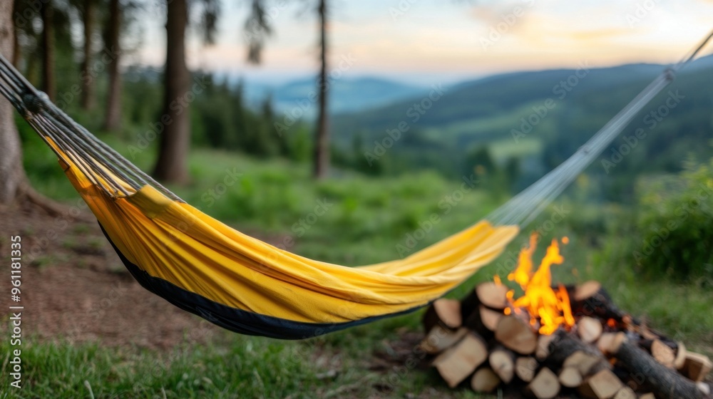 A vibrant yellow hammock hangs between trees near a crackling campfire, showcasing a serene mountain landscape as dusk falls, inviting relaxation and warmth A vibrant yellow hammock hangs between trees near a crackling campfire, showcasing a serene mountain landscape as dusk falls, inviting relaxation and warmth