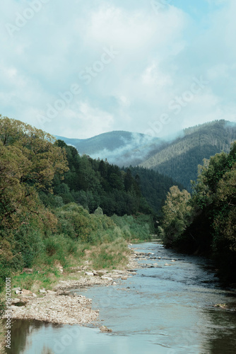 Tranquil river winding through lush valleys and misty mountains in a serene natural landscape under cloudy skies