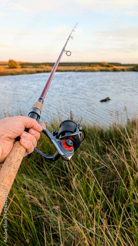 Hand holding fishing rod and reel, fishing at Corrib river at Galway, Ireland, spinning, angling, catch and release, sport and leisure, nature background