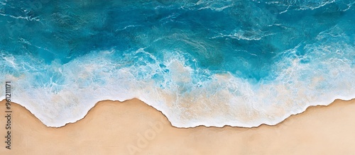 Aerial view of a sandy beach with turquoise water and white foamy waves crashing on the shore.