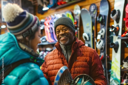 Senior man is smiling while shopping for a snowboard and talking with a salesperson in a sporting goods store