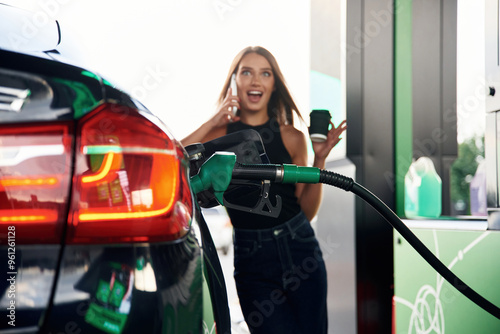 Talking by a phone. A young woman at a gas station with her car