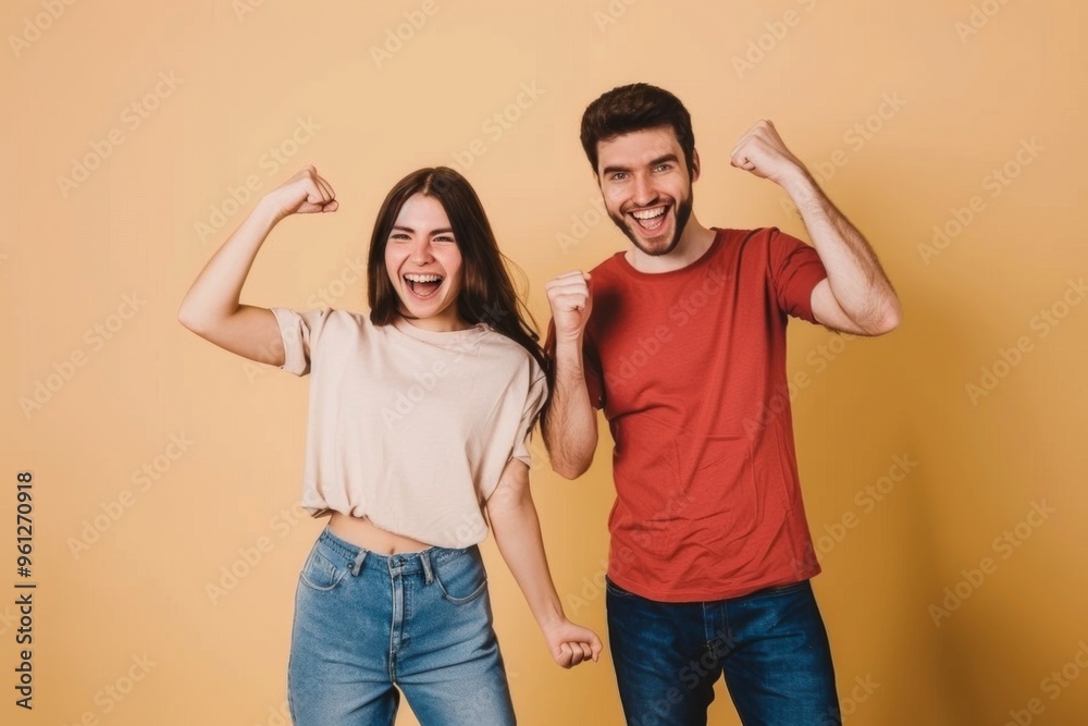 Fototapeta premium Two joyful friends celebrating together in casual outfits against a light beige background, capturing a moment of happiness and connection