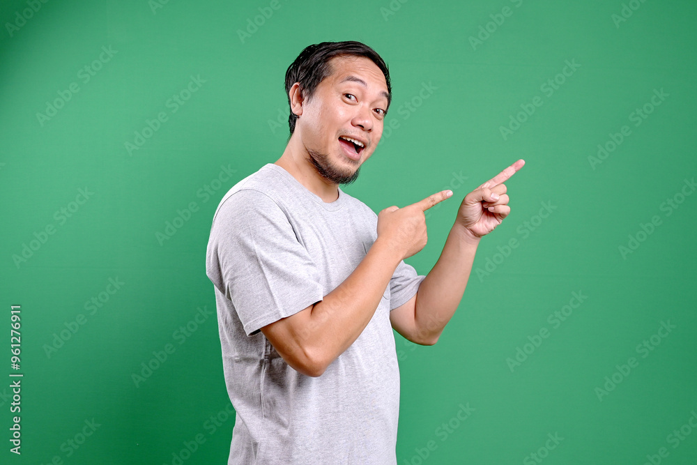 Happy young Asian man pointing fingers to the side presenting the product advertisement Happy young Asian man pointing fingers to the side presenting the product advertisement