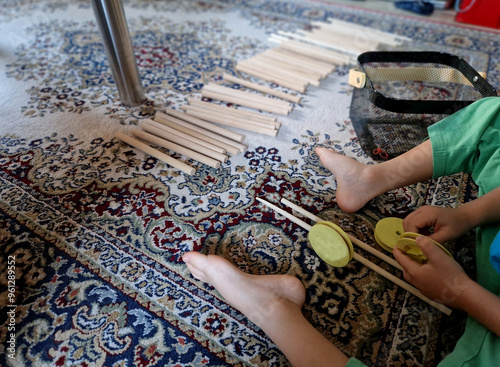 a child sorts wooden sticks on a Persian carpet. although it is a game it looks like child labor in less developed countries. his feet and hands are bare. puts things in a wire basket. ruffled carpet photo