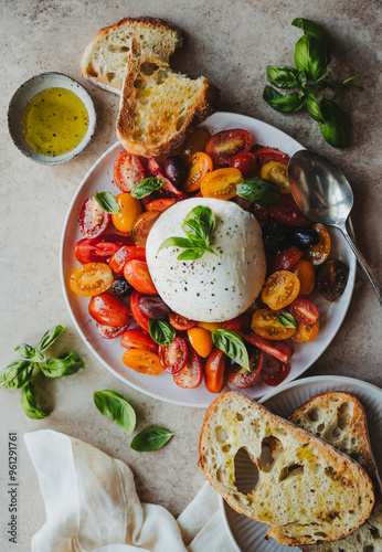 Overhead of plates of burrata cheese, tomatoes, basil and bread. photo