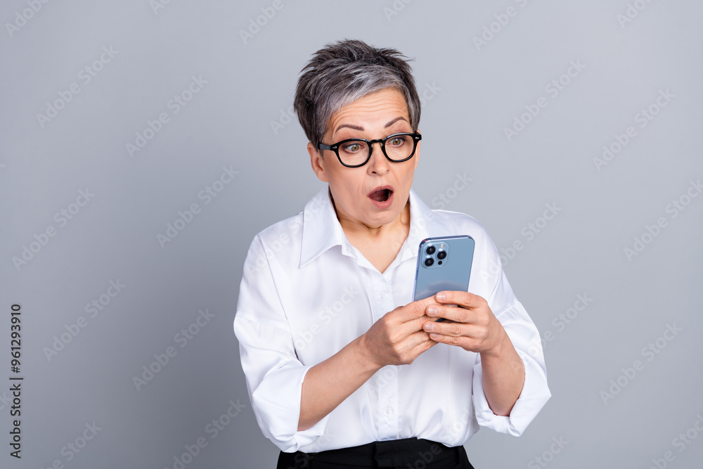 Photo portrait of attractive pensioner woman amazed hold gadget dressed stylish formalwear isolated on gray color background Photo portrait of attractive pensioner woman amazed hold gadget dressed stylish formalwear isolated on gray color background
