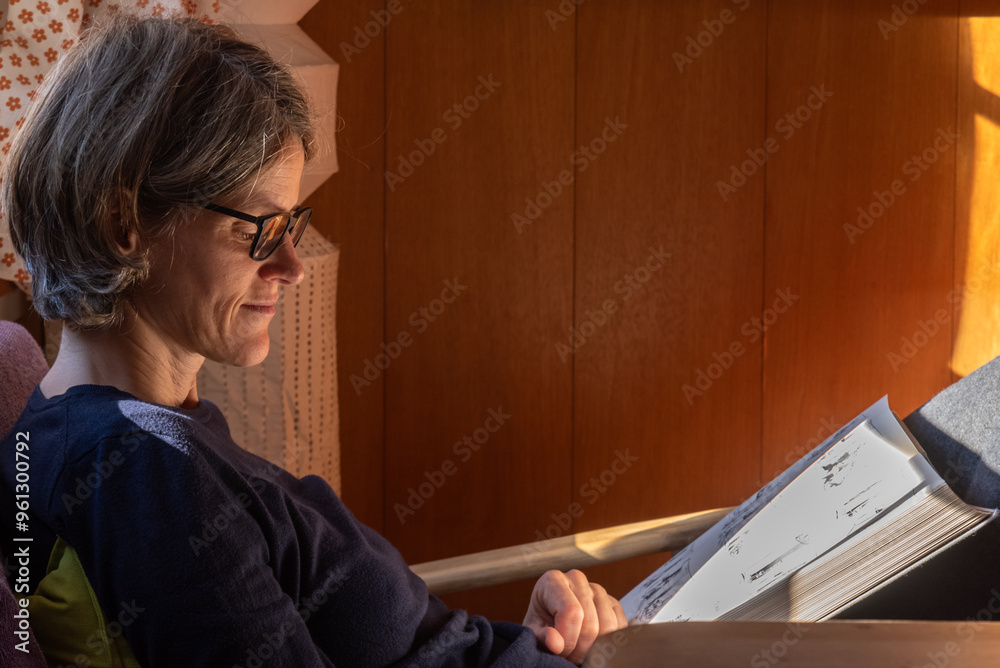 a woman reading a book with illustrations with the morning sunlight passing through the window
