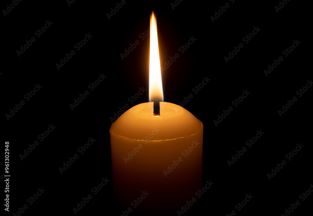A single burning candle flame or light glowing on a big white candle isolated on red or dark background on table in church for Christmas, funeral or memorial service A single burning candle flame or light glowing on a big white candle isolated on red or dark background on table in church for Christmas, funeral or memorial service