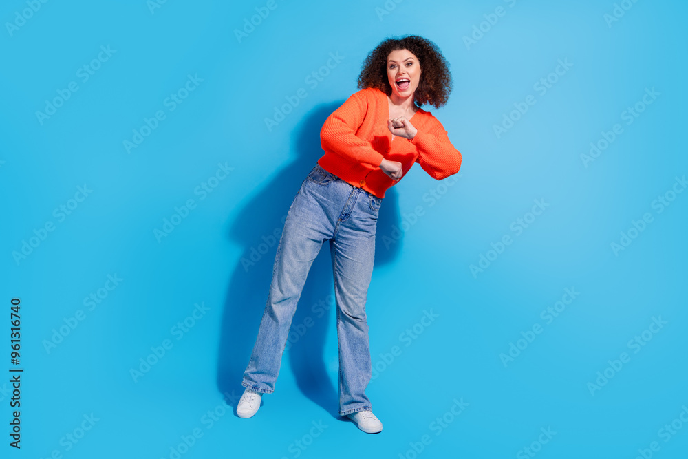 Photo portrait of young latin funny lady with curly hairstyle in orange cardigan dancing night club shaking hands isolated on blue color background Photo portrait of young latin funny lady with curly hairstyle in orange cardigan dancing night club shaking hands isolated on blue color background