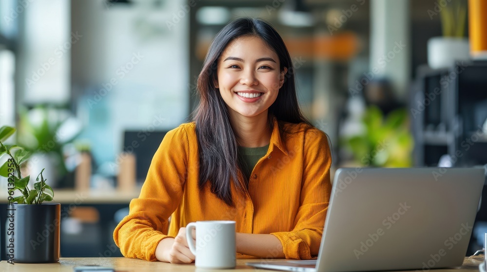 Smiling Woman in Yellow Shirt Working on Laptop at Modern Office with Coffee Mug Smiling Woman in Yellow Shirt Working on Laptop at Modern Office with Coffee Mug
