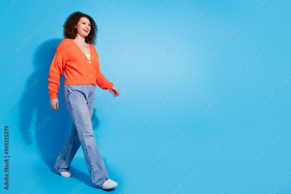 Photo portrait of wavy haired model woman wearing orange cardigan and jeans going into advertisement isolated on blue color background Photo portrait of wavy haired model woman wearing orange cardigan and jeans going into advertisement isolated on blue color background