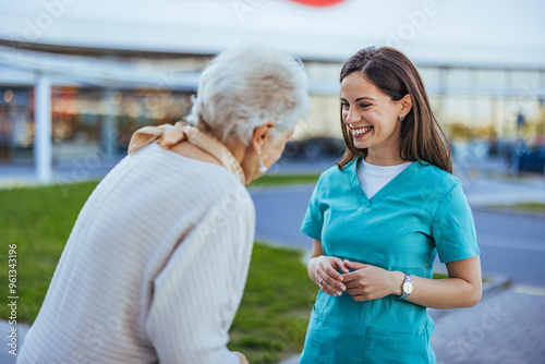 Smiling Nurse Assisting Elderly Woman Outdoors in Hospital Yard