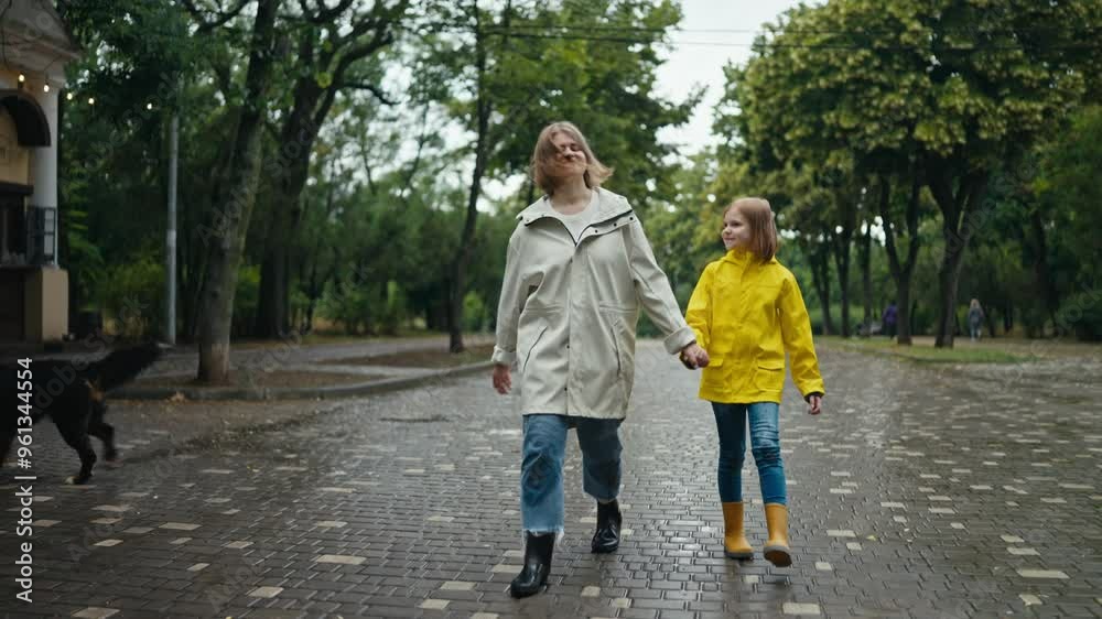 Happy blonde woman walks along the alley with her teenage daughter in a yellow jacket and talks along the alley in the park with a dog after the rain Happy blonde woman walks along the alley with her teenage daughter in a yellow jacket and talks along the alley in the park with a dog after the rain