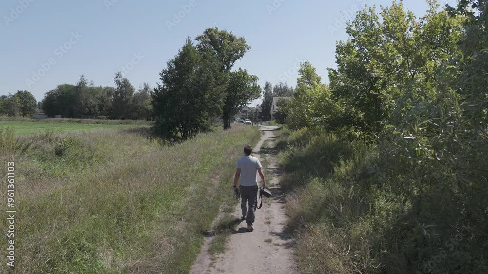 A man in linen pants and a light shirt walks with his dog through fields and trees, a bag on his shoulder, enjoying a sunny, clear sky. A man in linen pants and a light shirt walks with his dog through fields and trees, a bag on his shoulder, enjoying a sunny, clear sky.