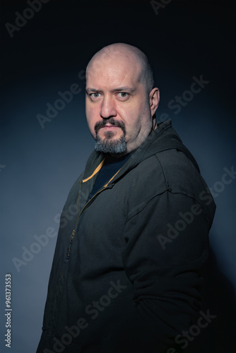 Mature bald man with goatee, dressed in black casual clothes on black background looking at camera with serious expression. Studio photography. Concept of man, maturity and baldness