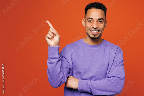 Young happy man of African American ethnicity wear purple sweatshirt casual clothes point index finger aside on area mockup isolated on plain red orange background studio portrait. Lifestyle concept. photo