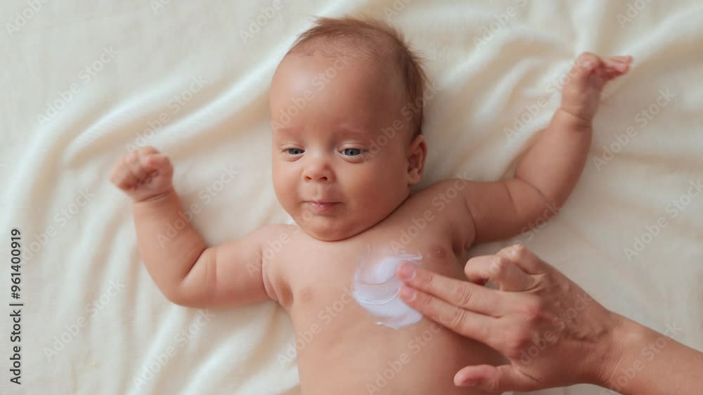 Nurturing mother skilled in massage therapy applying hydrating lotion to her baby’s delicate chest ensuring optimal skin moisture newborn baby lying on white sheet Nurturing mother skilled in massage therapy applying hydrating lotion to her baby’s delicate chest ensuring optimal skin moisture newborn baby lying on white sheet
