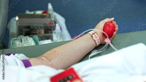 Female donor squeezing a red rubber heart to make blood flow faster. Medic at backdrop is getting ready to take blood. photo