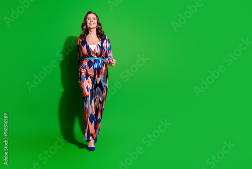 Full length photo of cheerful pretty lady dressed print outfiit walking empty space isolated green color background photo