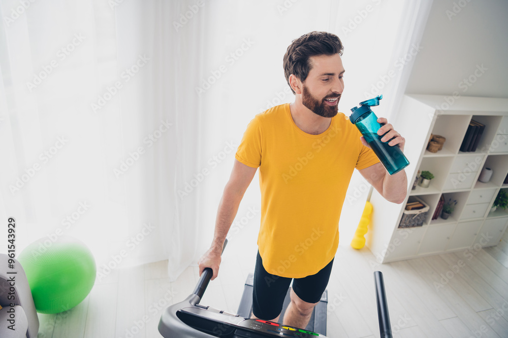 Photo of attractive strong man physical exercises running treadmill drinking water indoors home gym Photo of attractive strong man physical exercises running treadmill drinking water indoors home gym