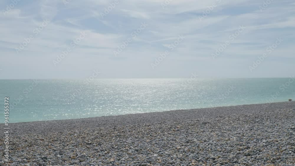 Elements of nature such as earth, air, and water are captured on a beach in Newhaven. Pebbles dot the shore as the calm sea stretches out with white clouds in the background. Elements of nature such as earth, air, and water are captured on a beach in Newhaven. Pebbles dot the shore as the calm sea stretches out with white clouds in the background.