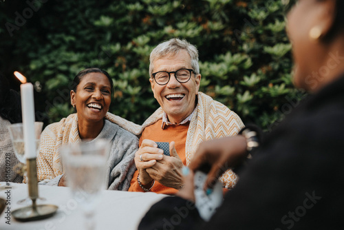 Cheerful senior man playing cards with family members at garden party